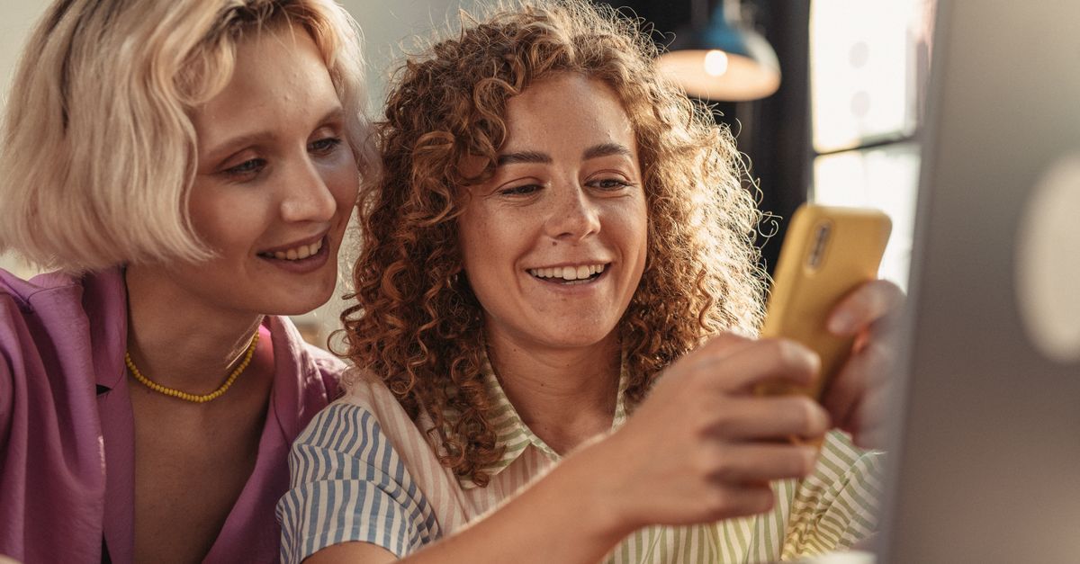 İki kadın telefon ekranına bakıp gülümseyerek fotoğraflara göz atıyor